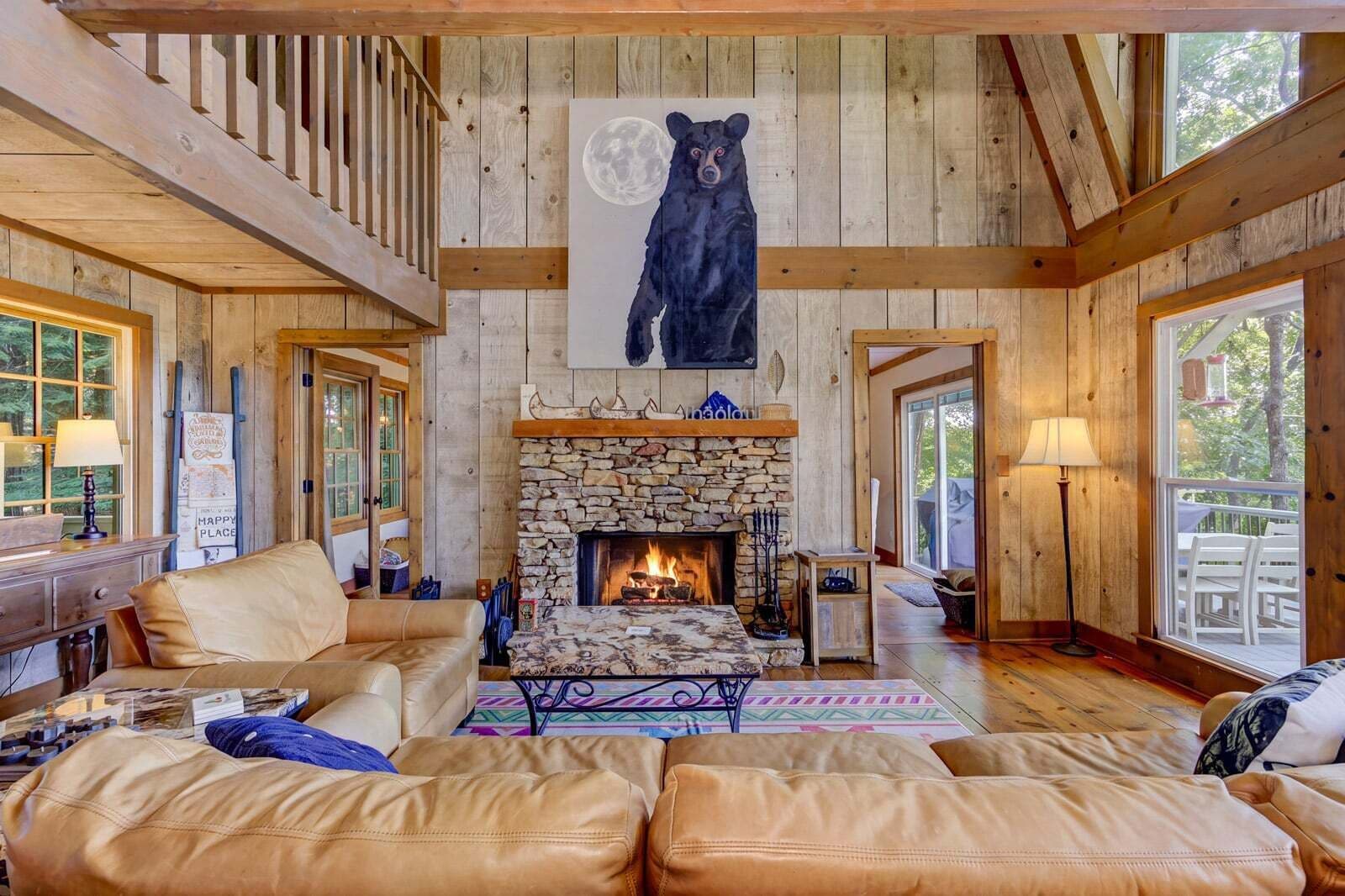 A cozy cabin interior with a stone fireplace, leather furniture, and a bear painting on the wall.