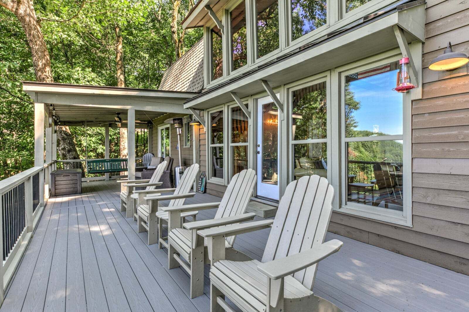 A covered deck with Adirondack chairs and a table, overlooking a forested area.