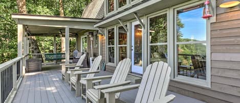 A covered deck with Adirondack chairs and a table, overlooking a forested area.