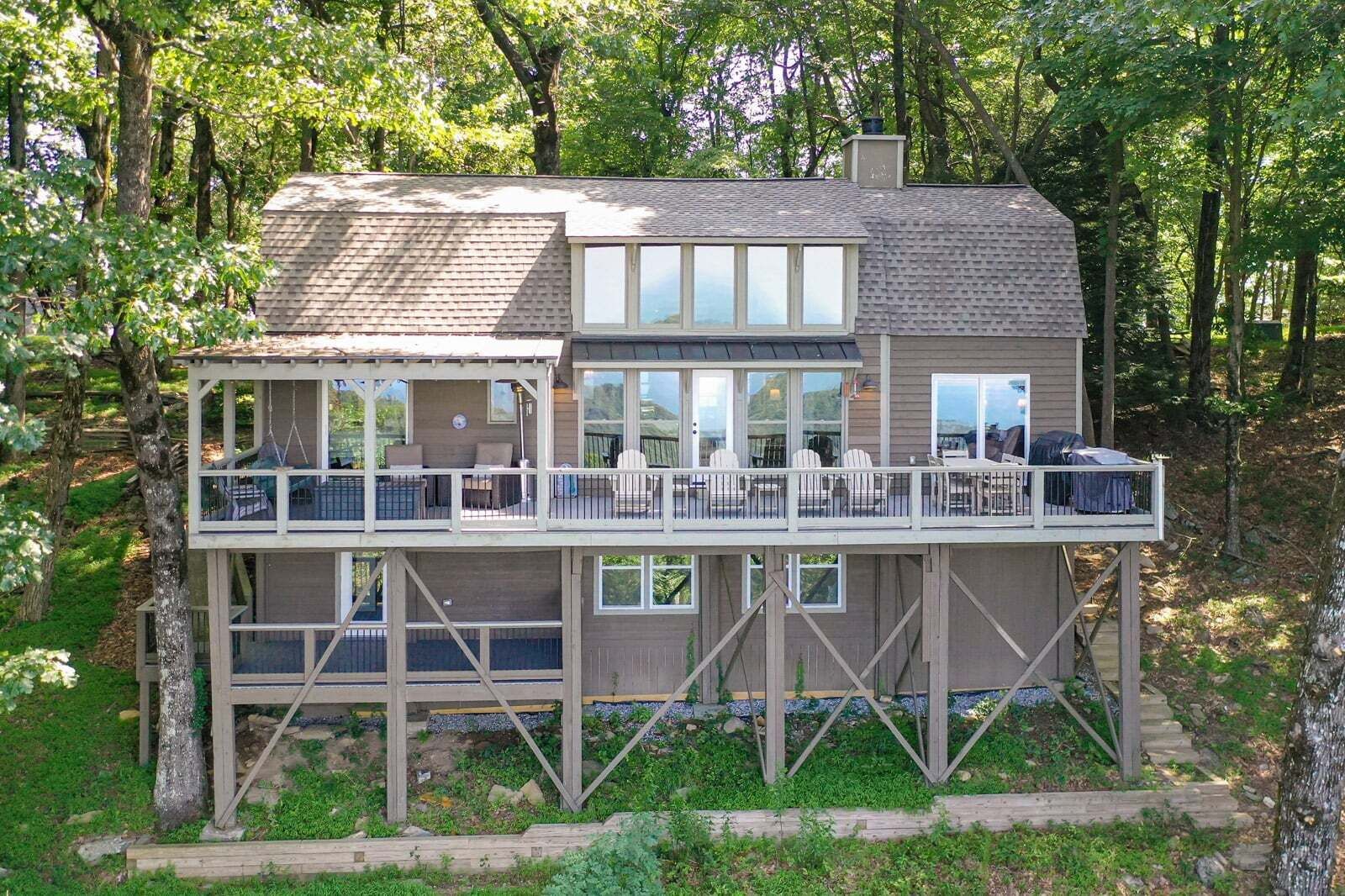 A two-story wooden cabin with a balcony, large windows, and a deck area.