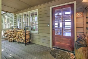 A wooden porch with a stack of firewood, a red door with glass panels, and a welcome mat. - Amazing Grace - Expansive Open-Air Deck, Long-Range Views + Big Canoe Access (Jasper)