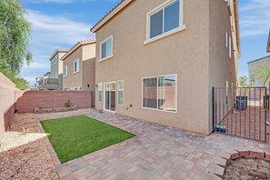 Un immeuble résidentiel doté d’une terrasse pavée, d’une petite pelouse et d’une entrée fermée par un portail.