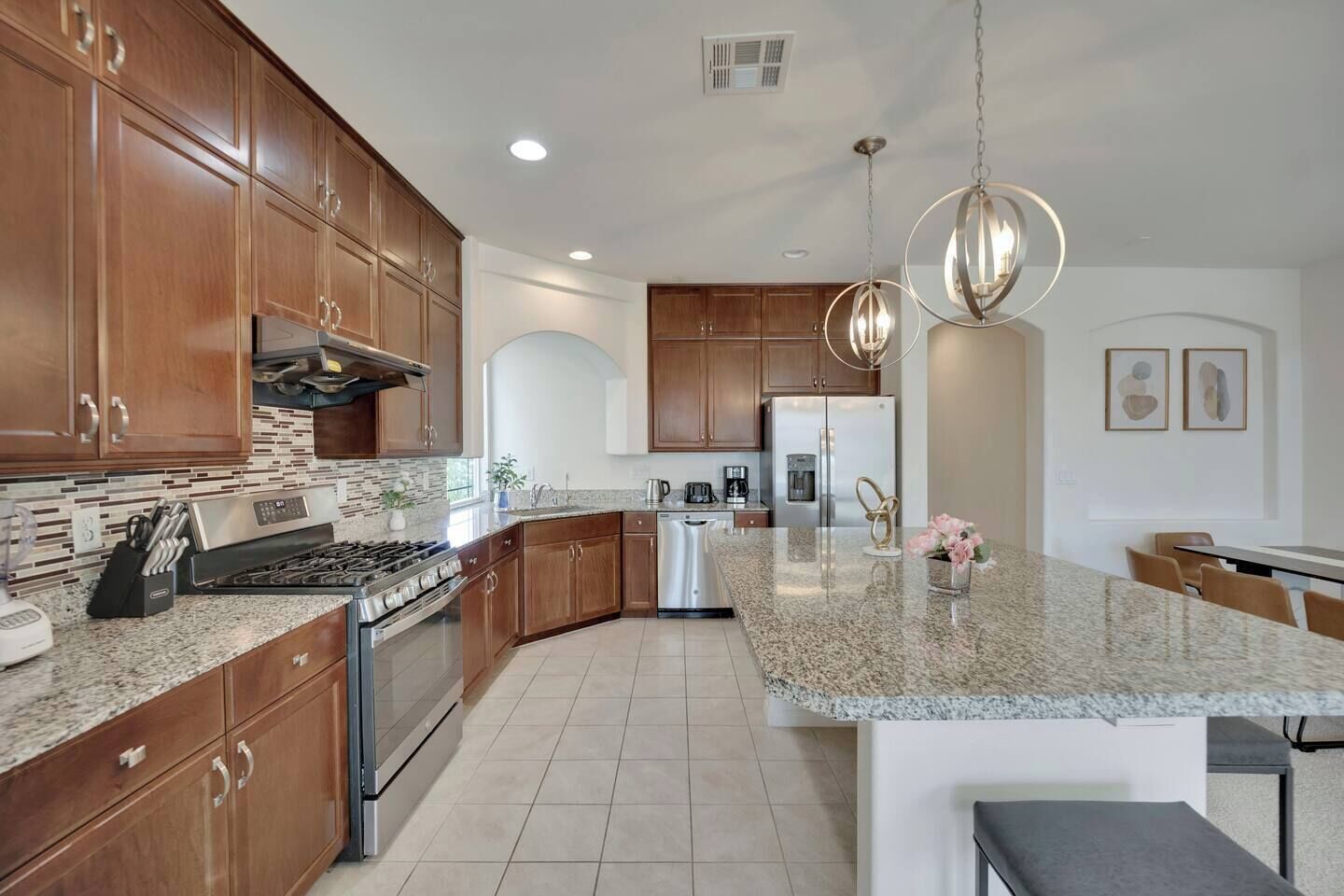 A modern kitchen with granite countertops, stainless steel appliances, wooden cabinets, and pendant lighting.