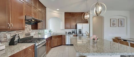 A modern kitchen with granite countertops, stainless steel appliances, wooden cabinets, and pendant lighting.