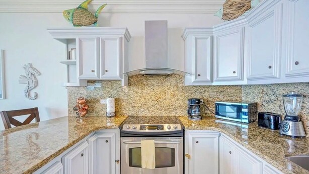 A kitchen with white cabinets, a granite countertop, a stove, a microwave, a toaster, and a blender. - 16th-Floor Oceanfront Condo with Stunning Sunset Views (Playas de Rosarito)