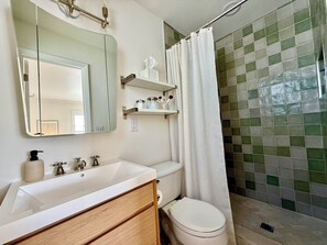 Un bagno con lavandino bianco, uno specchio, un water e una doccia con rivestimento a piastrelle verdi.