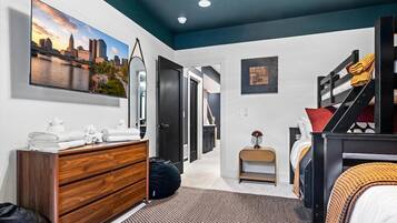 A bedroom with a cityscape painting, a wooden dresser, a bed with a patterned bedspread, and a staircase.