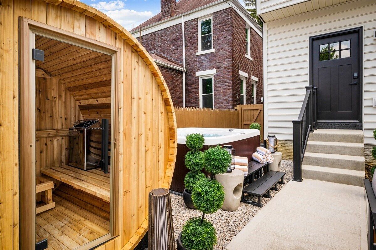 Una sauna con fachada de madera, un jacuzzi y un pequeño jardín con plantas en macetas.