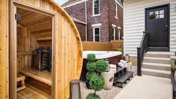 A sauna with a wooden exterior, a hot tub, and a small garden area with potted plants.