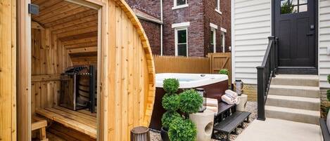 Una sauna con fachada de madera, un jacuzzi y un pequeño jardín con plantas en macetas.