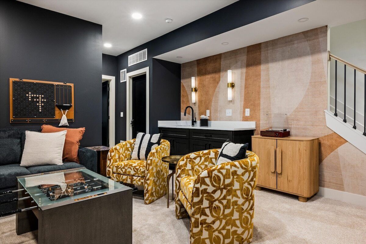 A modern living room with a sofa, armchairs, a coffee table, and a kitchen area with a sink and cabinets.