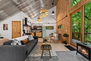 A modern interior with a sofa, dining table, and a fireplace. - Treeangle Treehouse - Romantic Treehouse for 2 | Firepit | Hot Tub (Morganton)