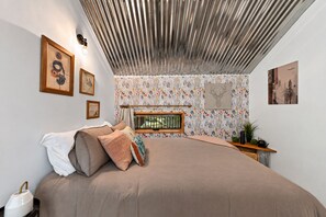 A bedroom with a bed, a window, and a wall with floral wallpaper. - Treeangle Treehouse - Romantic Treehouse for 2 | Firepit | Hot Tub (Morganton)