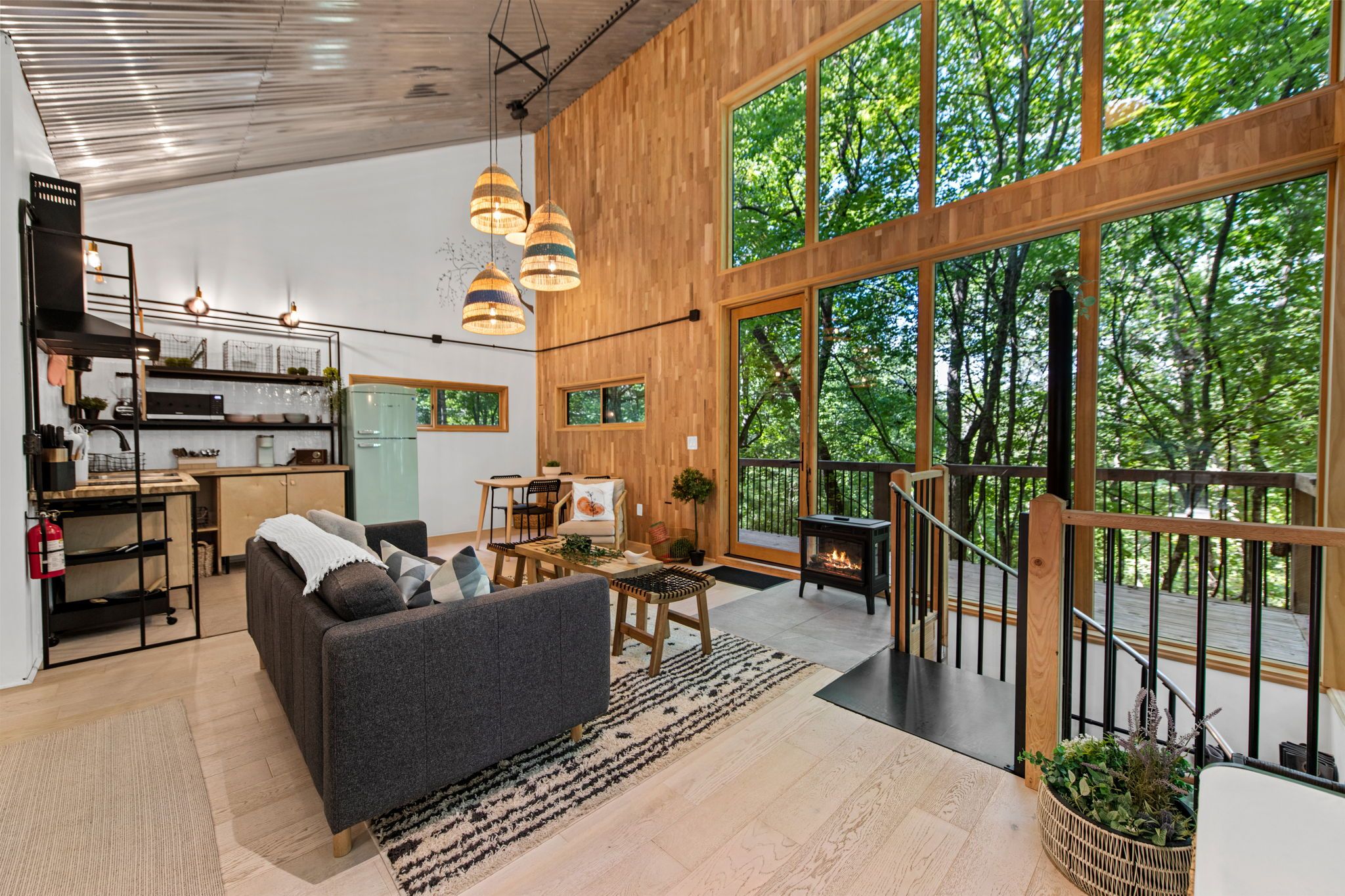 Et moderne interiør med sofa, spisebord og store vinduer med udsigt til en skov.