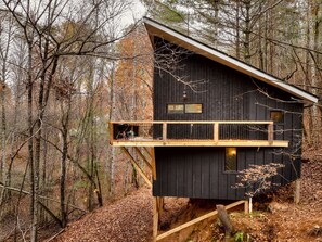 A cabin with a wooden deck and a balcony, surrounded by a forest. - Treeangle Treehouse - Romantic Treehouse for 2 | Firepit | Hot Tub (Morganton)