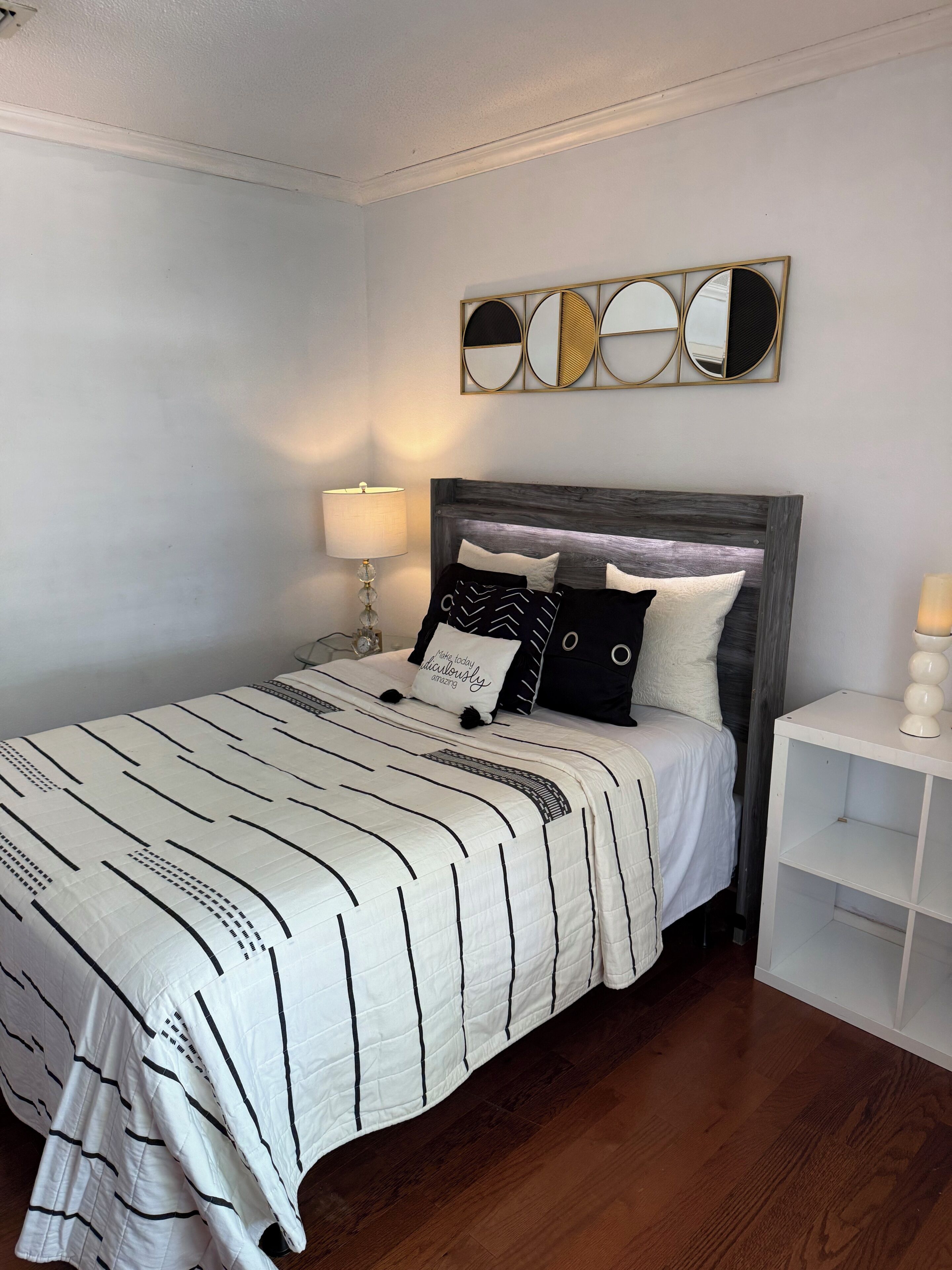 Ein ordentlich gemachtes Bett mit gestreifter Bettdecke, ein Nachttisch mit Lampe und ein wandmontierter Spiegel.