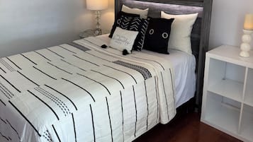 Ein ordentlich gemachtes Bett mit gestreifter Bettdecke, ein Nachttisch mit Lampe und ein wandmontierter Spiegel.