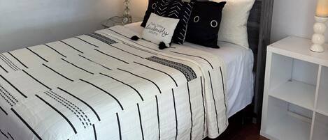 A neatly made bed with a striped bedspread, a bedside table with a lamp, and a wall-mounted mirror.