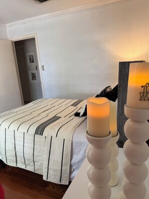 Een slaapkamer met een bed, een nachtkastje met kaarsen, en een deur naar een andere kamer.