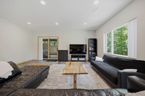 A modern living room with a sofa, a coffee table, a TV, and a bookshelf. - Charming Getaway - Cozy Retreat in Logan with Hot Tub (Logan)
