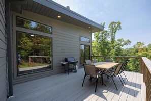 Een modern terras met een tafel, stoelen, een barbecue en uitzicht op de omliggende bomen.
