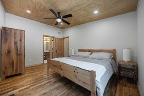 A bedroom with a wooden bed, a ceiling fan, and a nightstand with a lamp. - Charming Getaway - Cozy Retreat in Logan with Hot Tub (Logan)