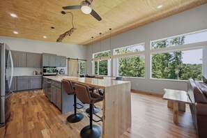 Una cocina moderna con suelo de madera, una isla central con taburetes de bar y amplias ventanas con vistas al exterior.