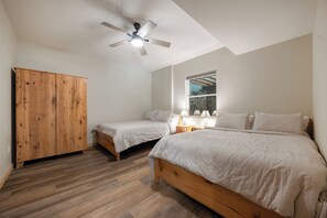 Een slaapkamer met twee bedden, een houten garderobe, een plafondventilator en een raam met uitzicht.