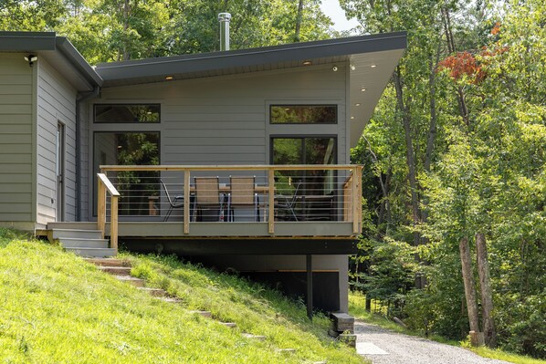 Een modern huis met twee verdiepingen, een balkon en uitzicht op het omliggende bos.