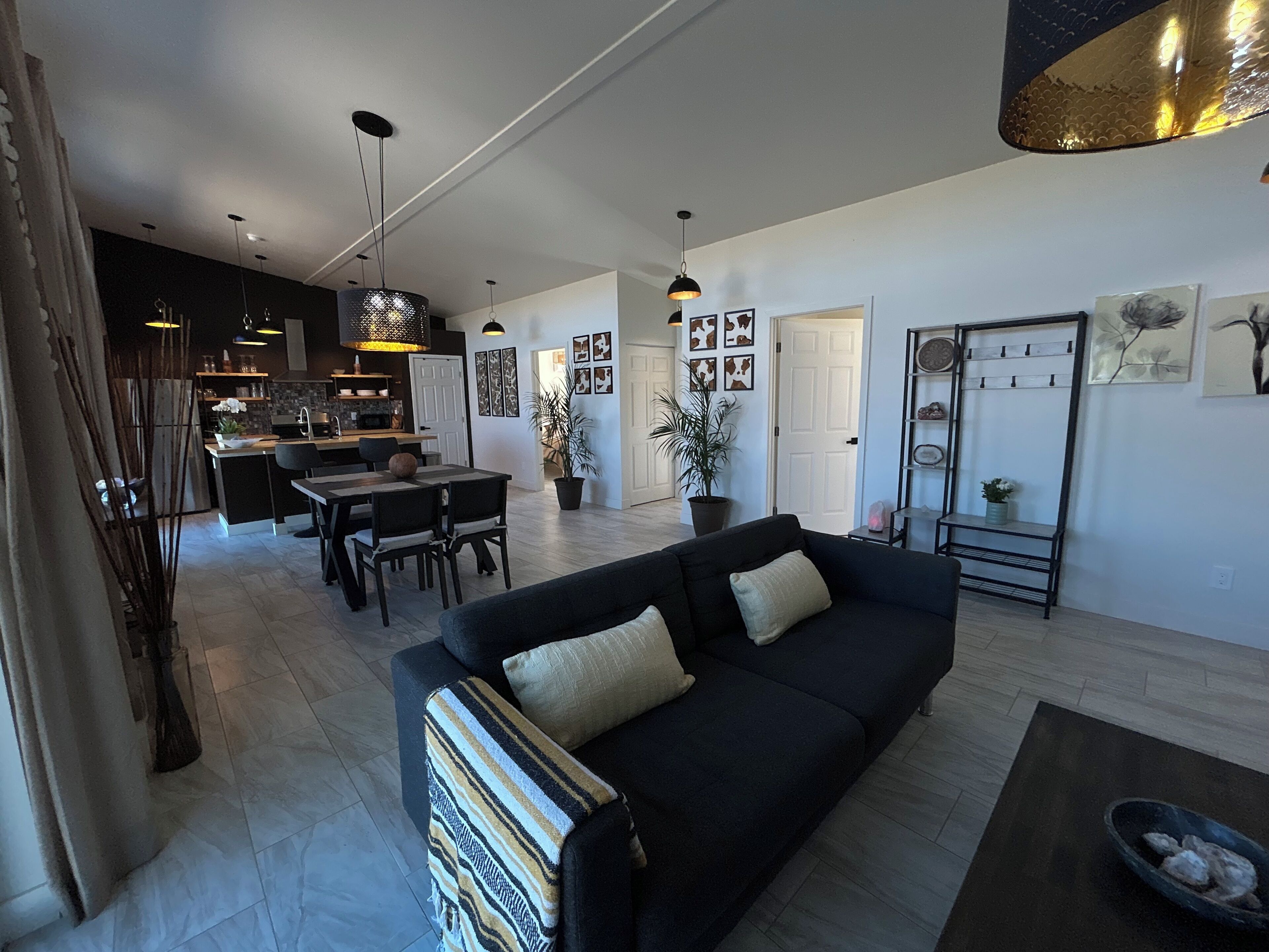 A modern living room with a black sofa, a dining area, and a kitchen in the background.
