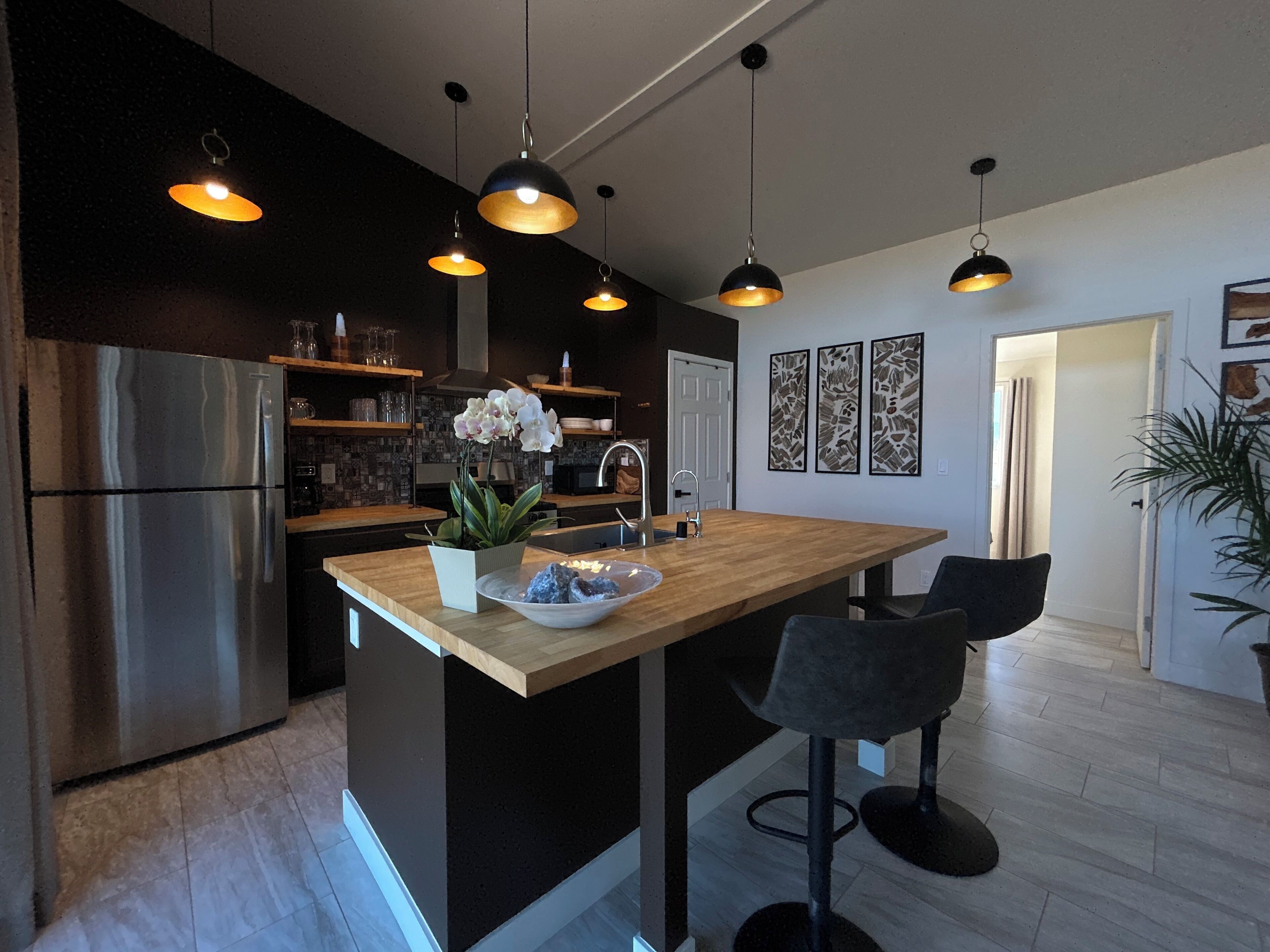A modern kitchen with a central island, stainless steel appliances, pendant lighting, and a view into the dining area.