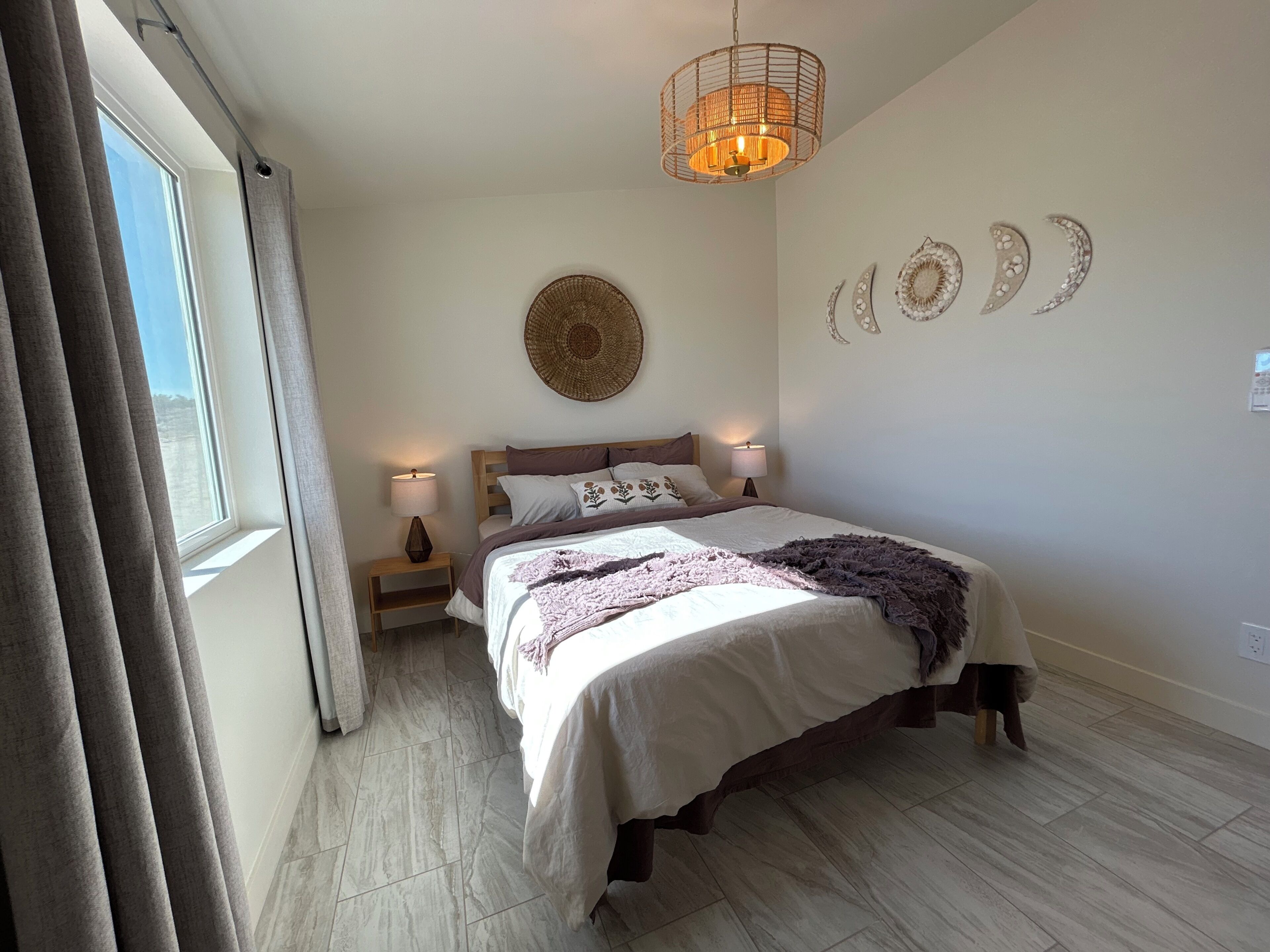 A bedroom with a bed, bedside lamps, a wall-mounted circular decoration, and a window with curtains.