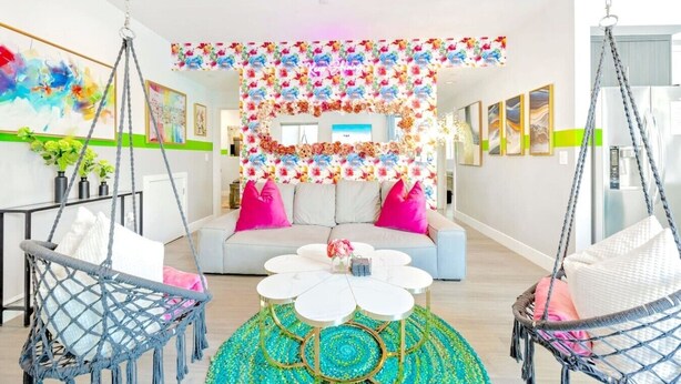 Un salon moderne avec un canapé, deux fauteuils suspendus, une table basse et une décoration murale à motifs floraux.