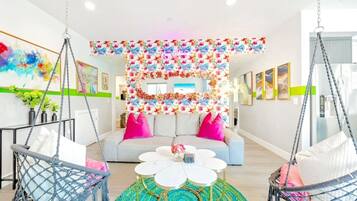 Un salon moderne avec un canapé, deux fauteuils suspendus, une table basse et une décoration murale à motifs floraux.