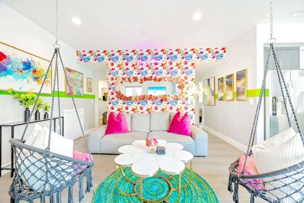 A modern living room with a sofa, two hanging chairs, a coffee table, and a floral wall decoration.