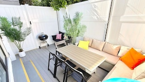 Un espace patio aménagé avec une table et des chaises, un canapé avec des coussins et des plantes en pot.