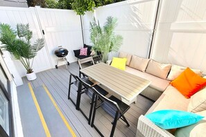 A patio area with a table and chairs, a sofa with cushions, and potted plants.
