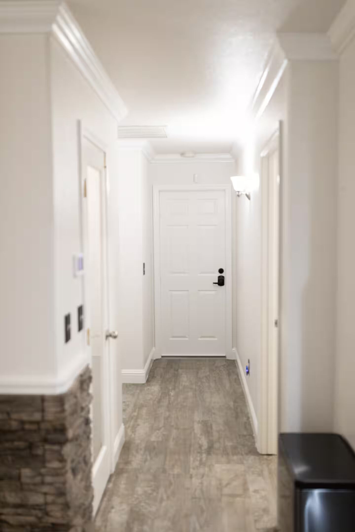 A hallway with a white door at the end, a stone accent wall, and a black trash bin.