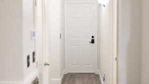 A hallway with a white door at the end, a stone accent wall, and a black trash bin.