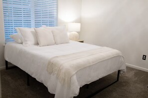 A bedroom with a bed, white bedding, a nightstand with a lamp, and a window with blinds. - Rustic Chateau/Estate -Pool, Spa, Tennis Court, and Quiet, Peaceful Surroundings (Del Rey)