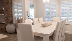 Un coin repas avec une table et des chaises blanches, un vase décoratif et un mur en briques.