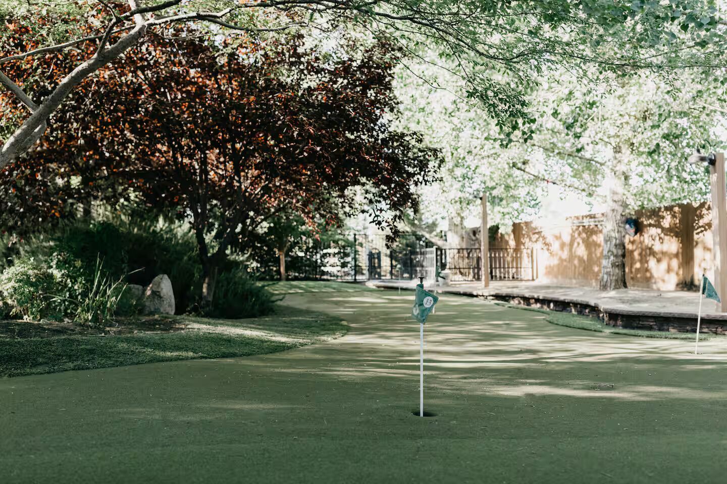 A golf course with a flagstick, trees, and a stone wall in the background.