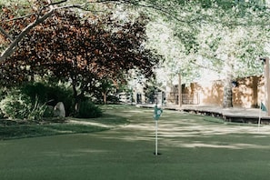 A golf course with a flagstick, trees, and a stone wall in the background.