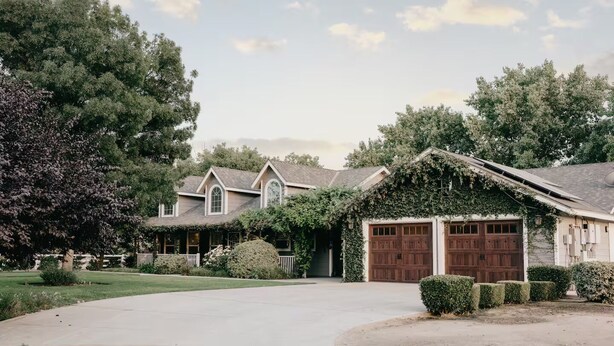 Une maison à deux étages avec un garage fermé, entourée d’une pelouse bien entretenue et d’arbres adultes.