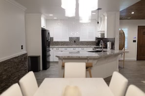 A modern kitchen with a central island, white cabinetry, and a dining area with a table and chairs.