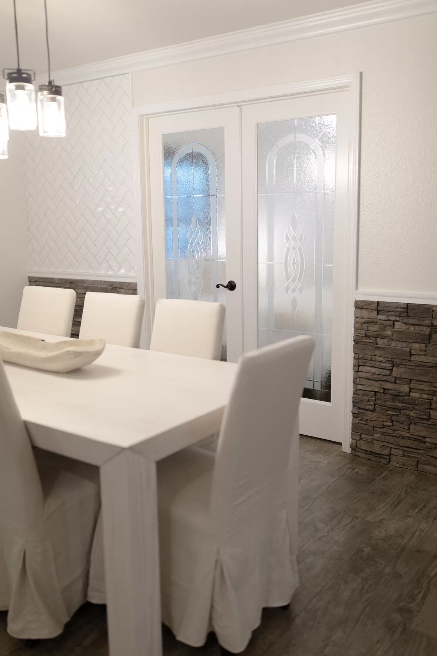 A dining area with a white table and chairs, a decorative bowl on the table, and a stone accent wall.
