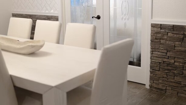 A dining area with a white table and chairs, a decorative bowl on the table, and a stone accent wall.