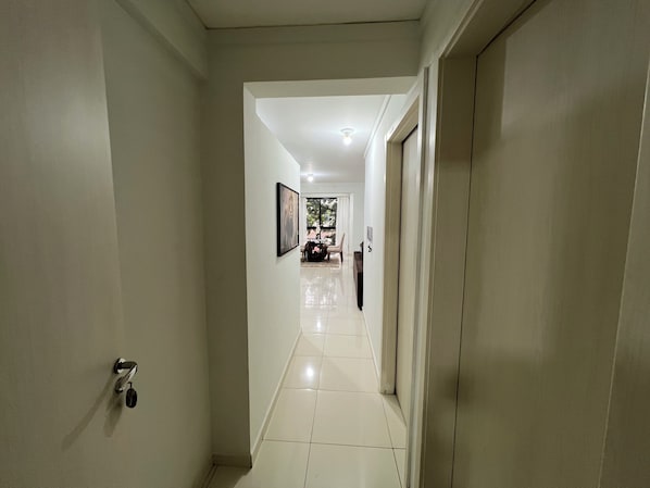 A hallway with a door on the left, a framed picture on the wall, and a glimpse of a living area at the end.