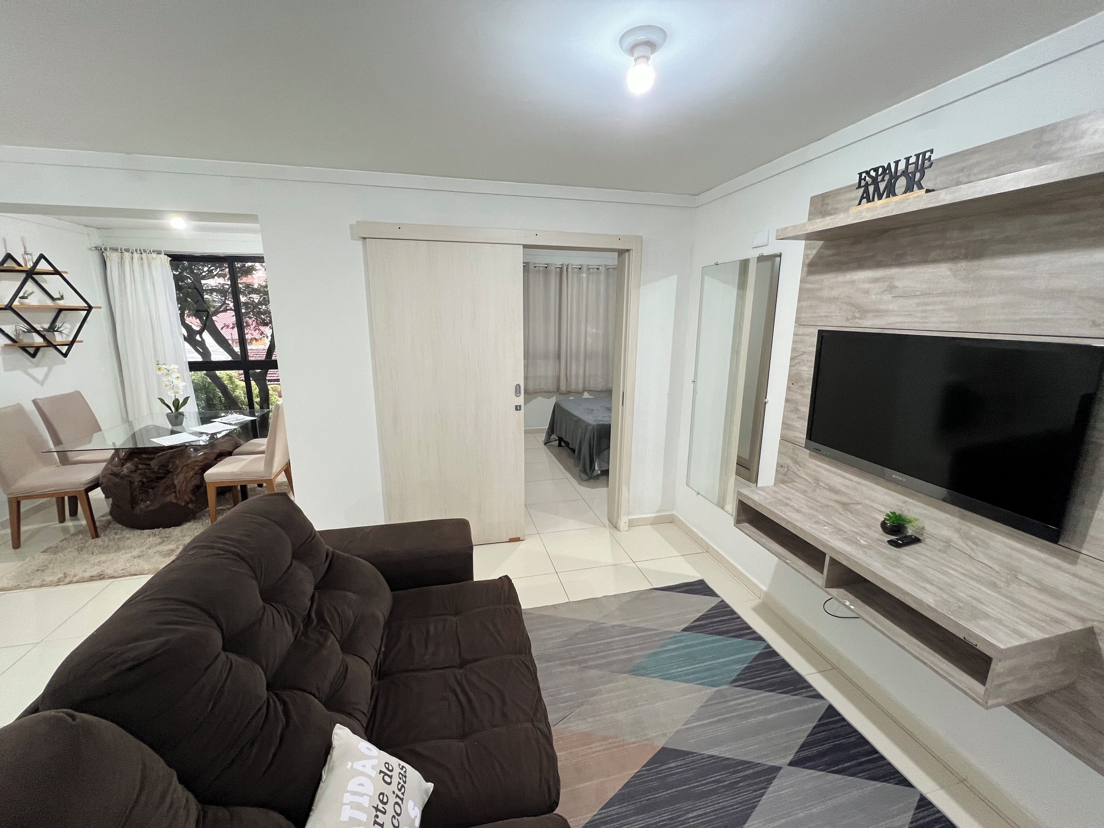 A modern living room with a large flat-screen TV, a dark brown sofa, and a patterned rug.