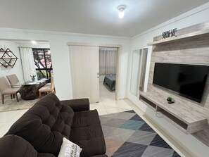 A modern living room with a large flat-screen TV, a dark brown sofa, and a patterned rug.